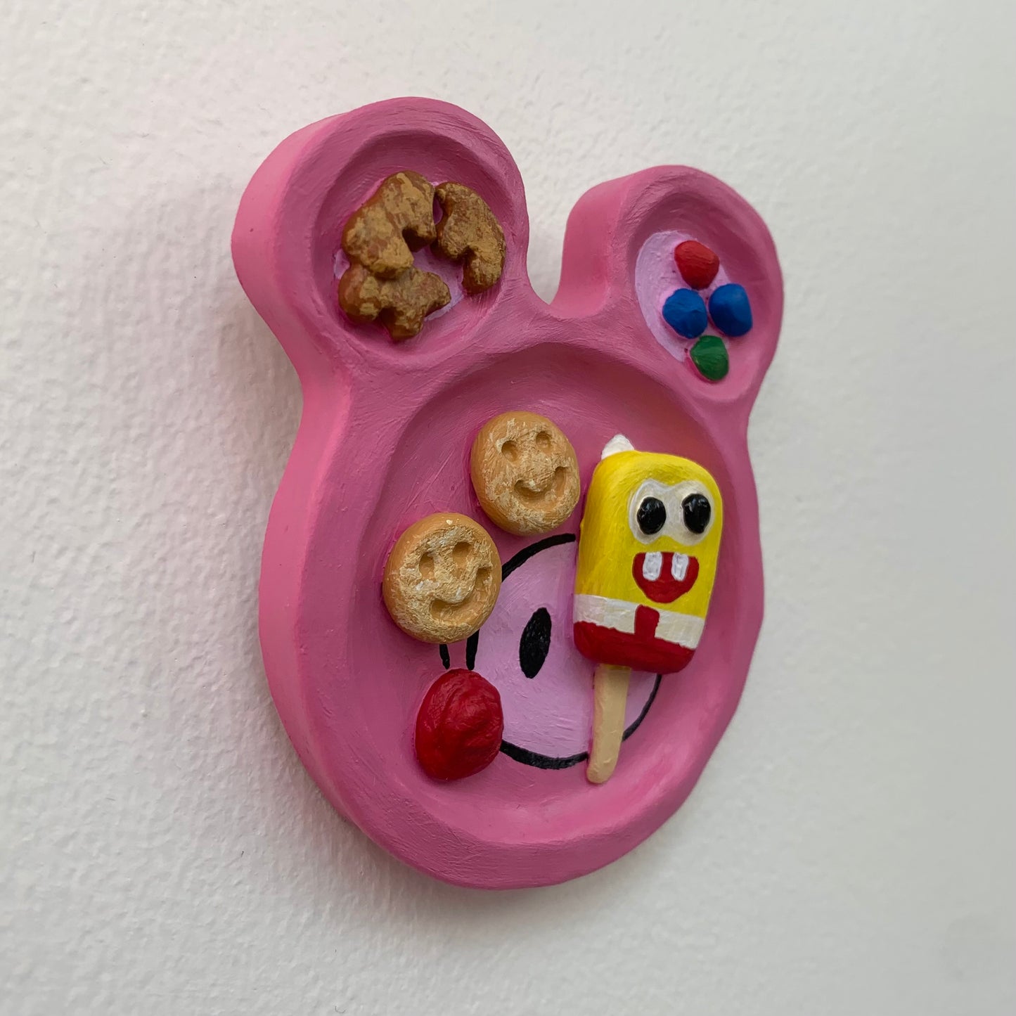 Pink mouse-shaped plate with cartoon character and snacks on a white background