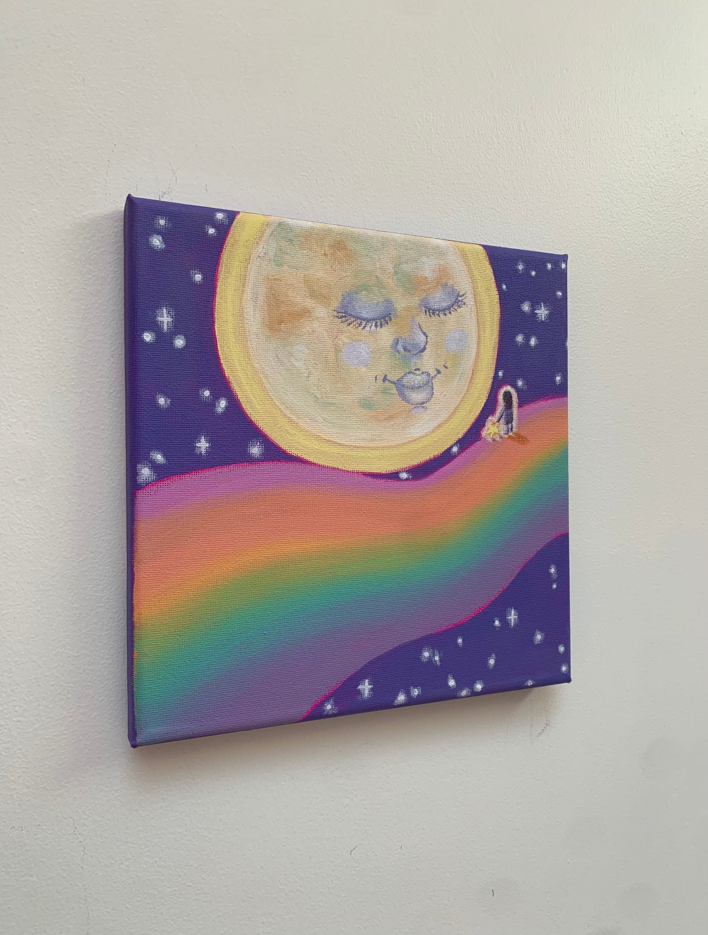 Canvas print with a colorful design of a rainbow, moon, and stars on a white wall.