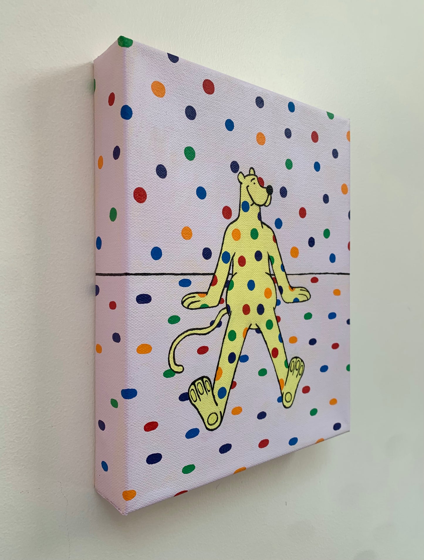 Canvas painting on a white wall of a yellow cartoon leopard character with rainbow polka dot pattern on a polka dot background sitting on the ground