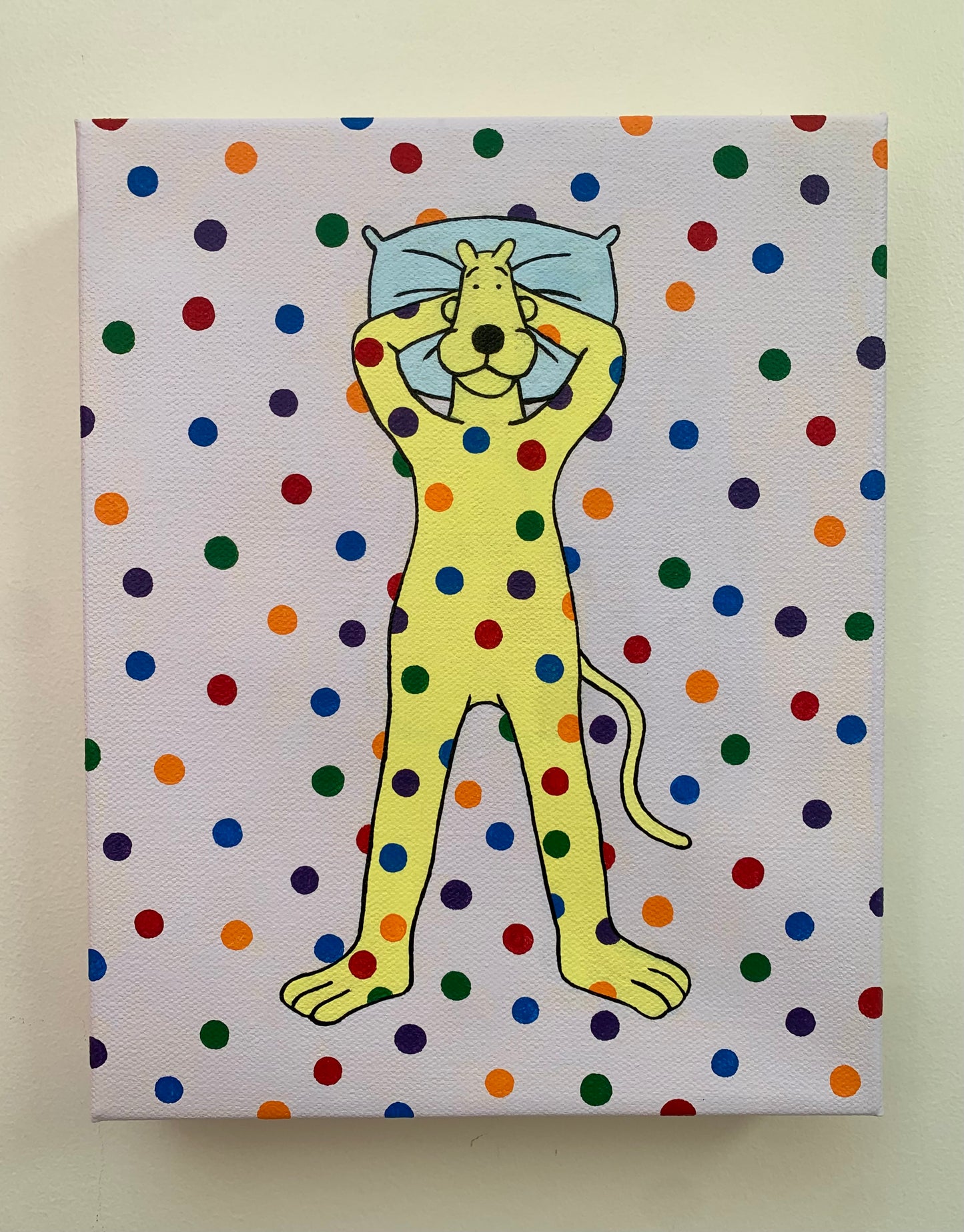 Canvas painting of a yellow cartoon leopard lying on the ground with his head on a pillow. Rainbow spots are all over him and the background