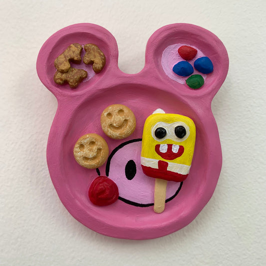 Pink plate shaped like a cartoon face with food items on a white background
