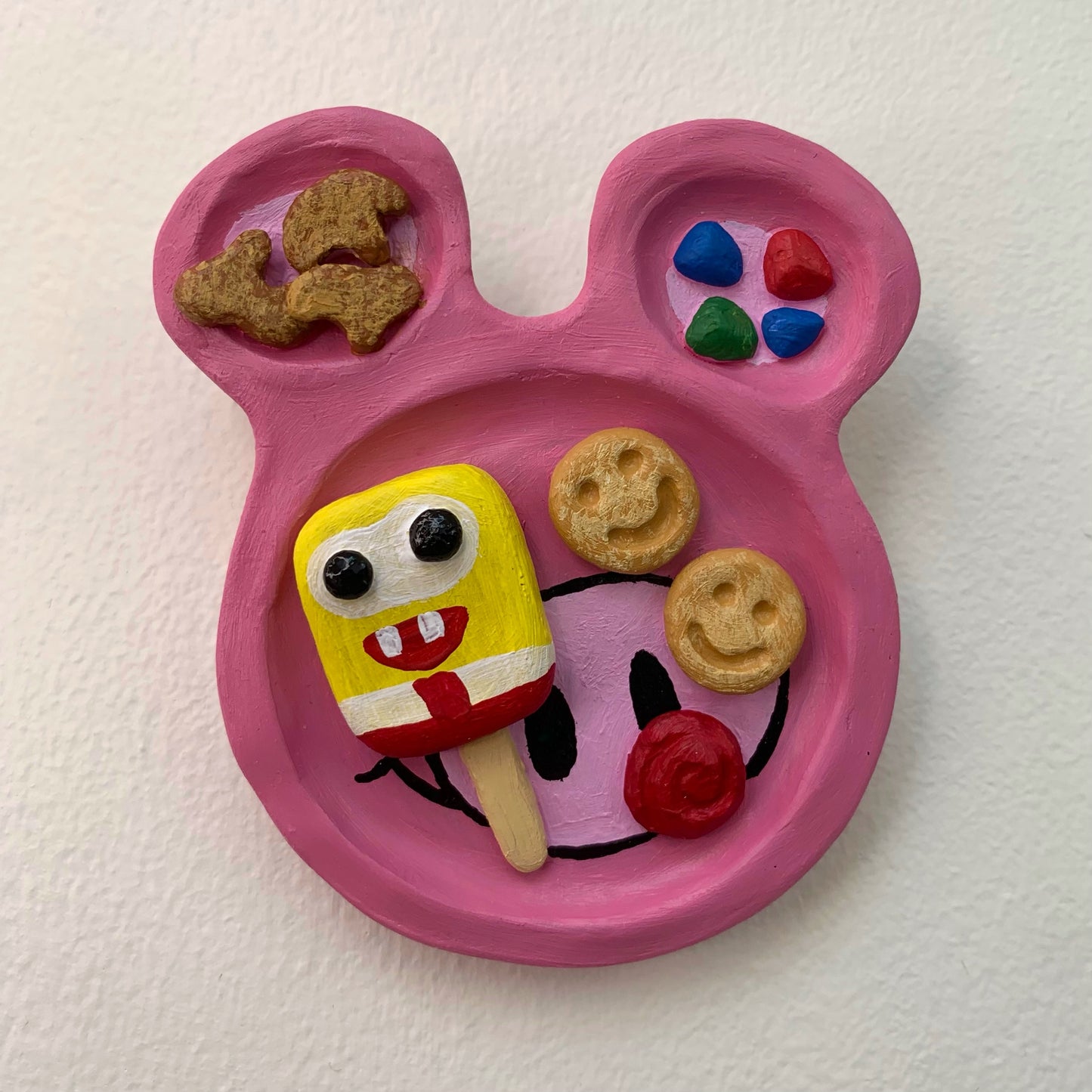 Pink mouse shaped sculpture on a white wall with rainbow dessert treats on the surface