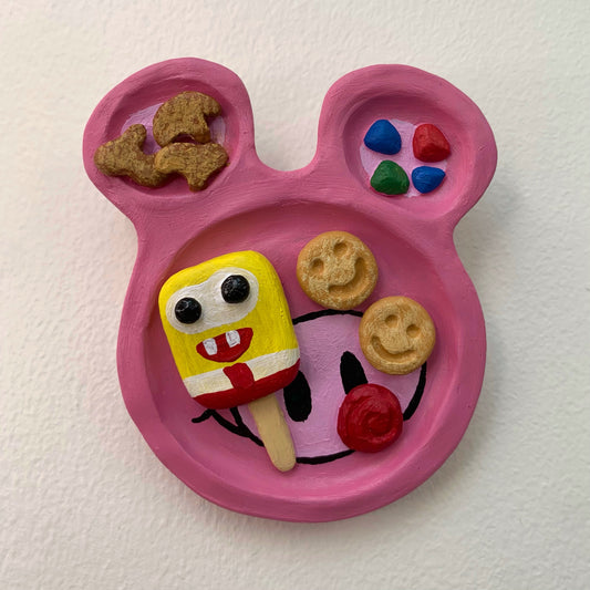 Pink mouse shaped sculpture on a white wall with rainbow dessert treats on the surface