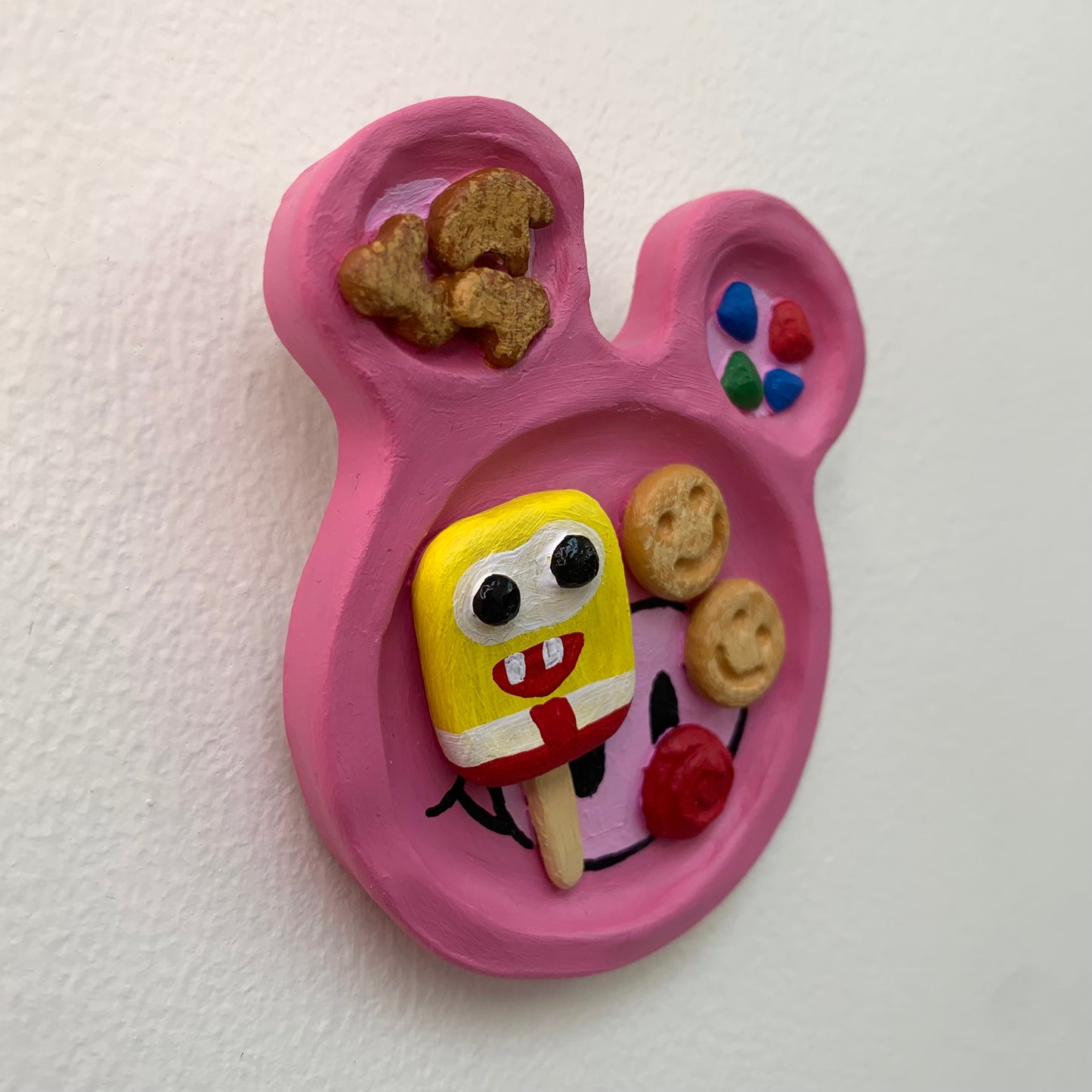 Pink mouse shaped sculpture on a white wall with rainbow dessert treats on the surface
