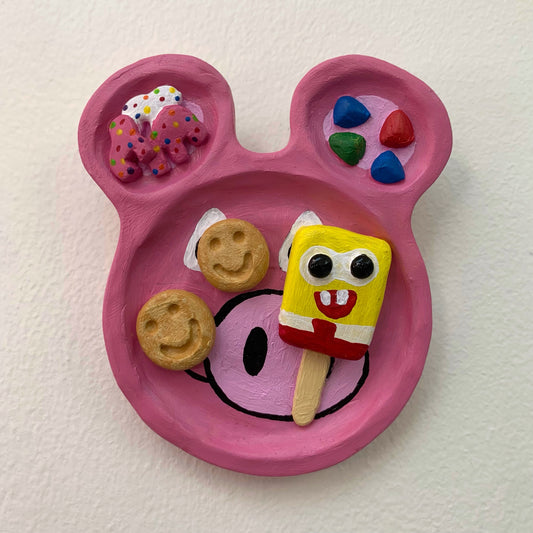 Pink plate shaped like a cartoon face with colorful items on a white background